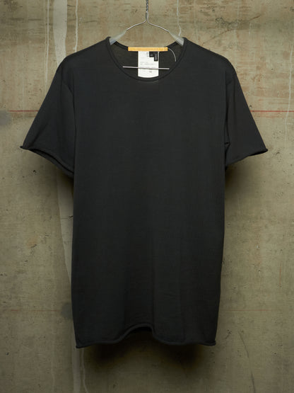 A plain black short-sleeve crewneck t-shirt hanging on a wire hanger against a textured concrete wall.