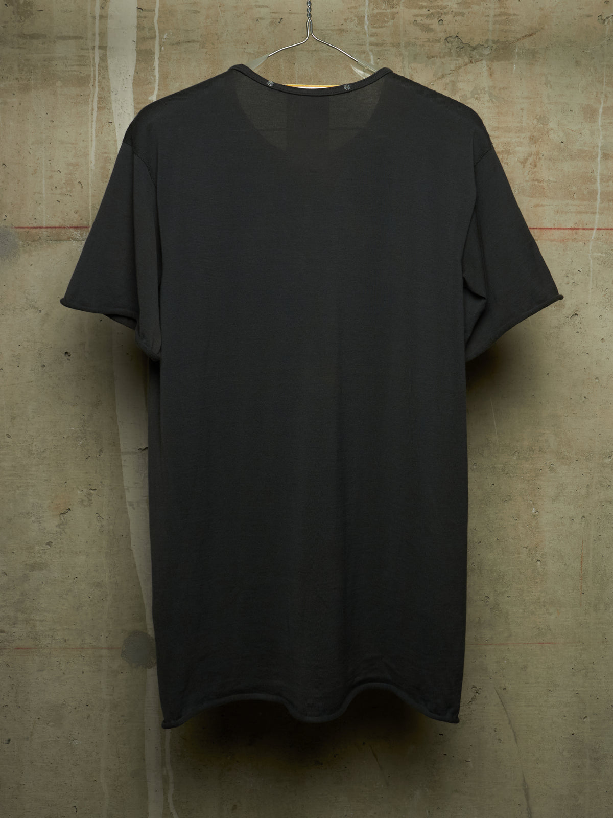 A plain black short-sleeve t-shirt hanging on a metal hanger against a textured concrete wall.