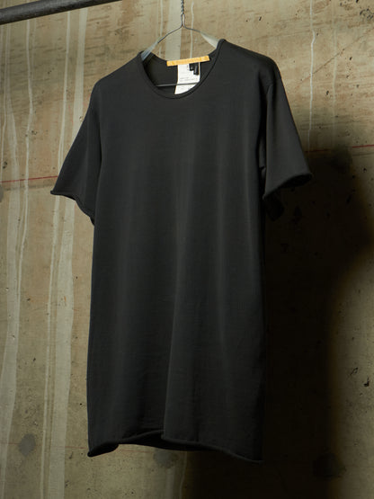 A black short-sleeve crewneck t-shirt hanging on a metal hanger against a textured concrete wall.