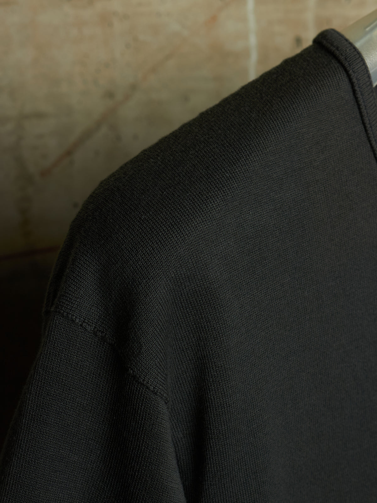 Close-up of a black ribbed knit garment, likely a sweater or sweatshirt, showing the shoulder and upper chest area against a warm beige background.