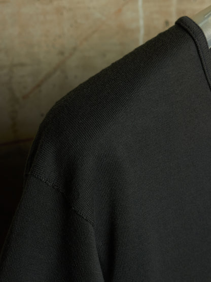 Close-up of a black ribbed knit garment, likely a sweater or sweatshirt, showing the shoulder and upper chest area against a warm beige background.