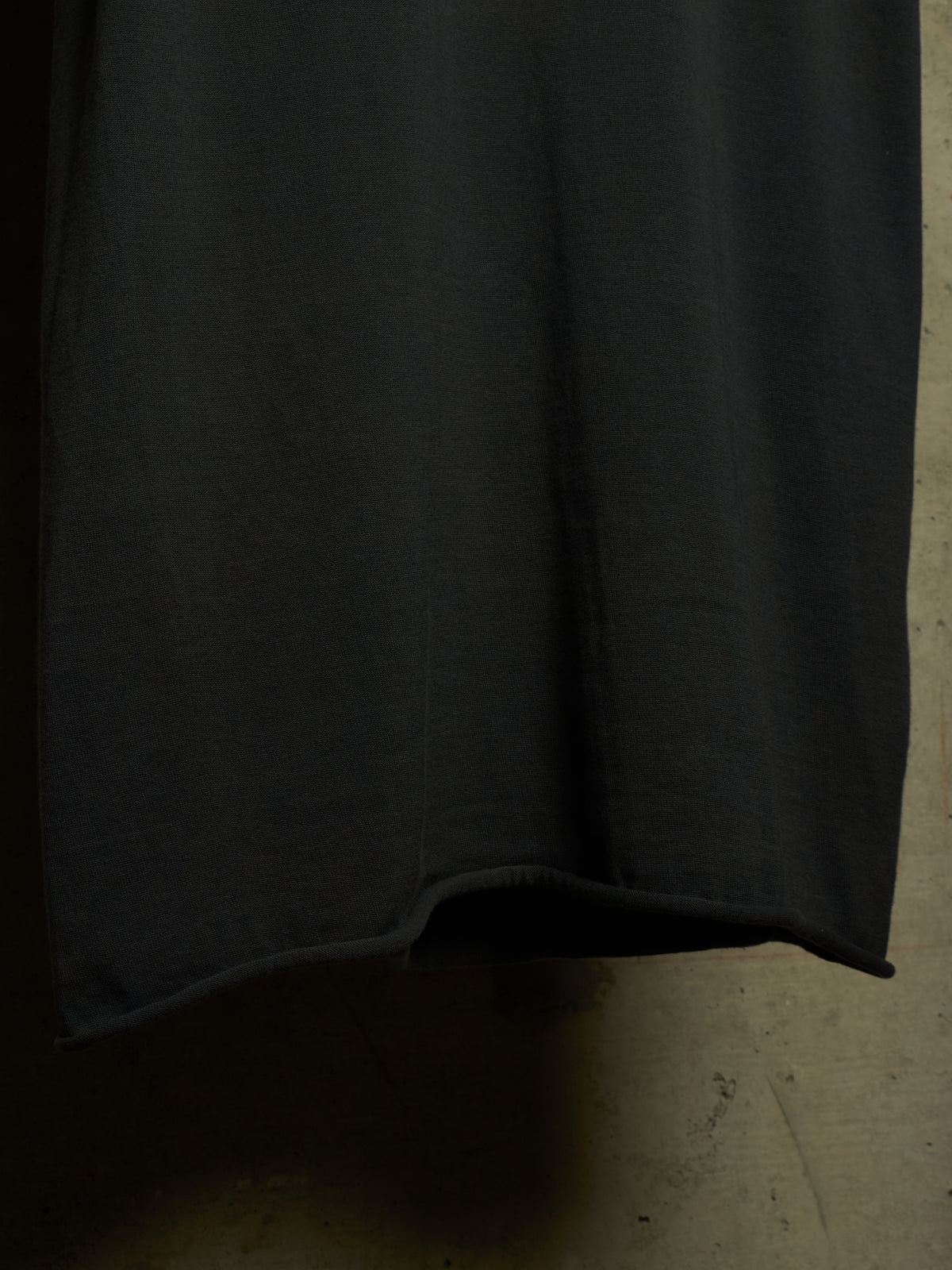 A close-up of a dark charcoal gray fabric, likely a skirt or drape, hanging against a textured concrete floor.