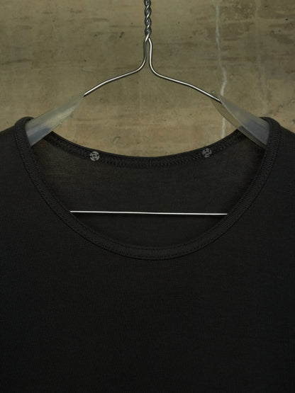 A close-up of a black crew-neck top hanging on a clear plastic hanger against a textured concrete wall.
