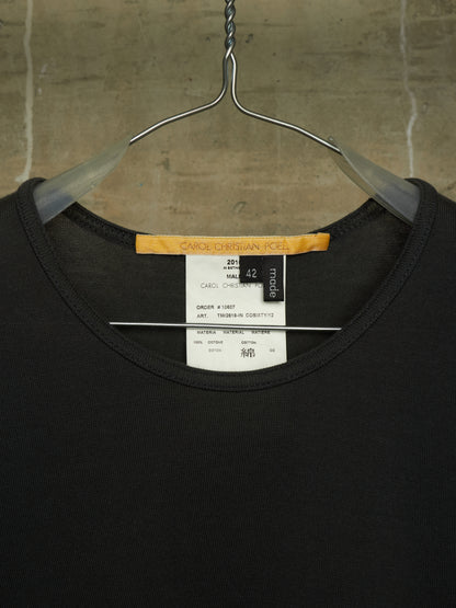 A black crewneck t-shirt hanging on a metal hanger against a textured concrete wall. The neck label shows the brand 'SACRED DESIGN CO.