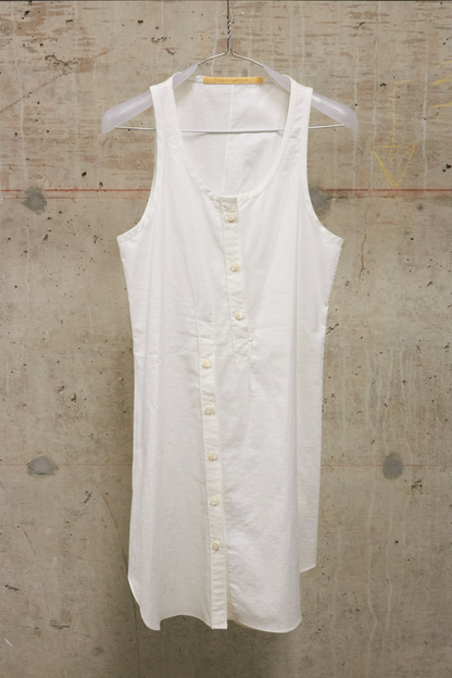 White sleeveless shirt on a hanger against a textured beige wall.