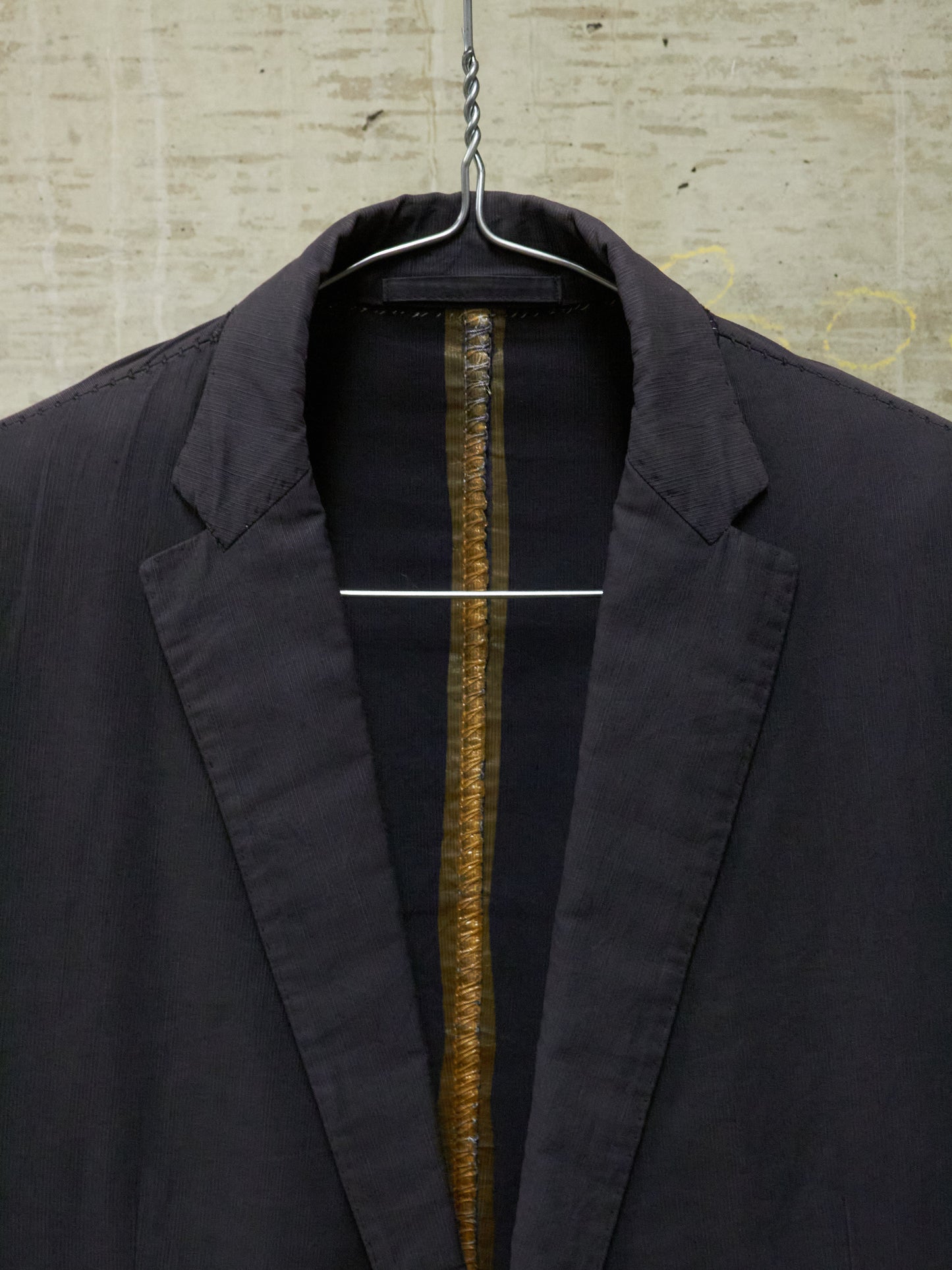 Black jacket on a hanger against a textured wall.