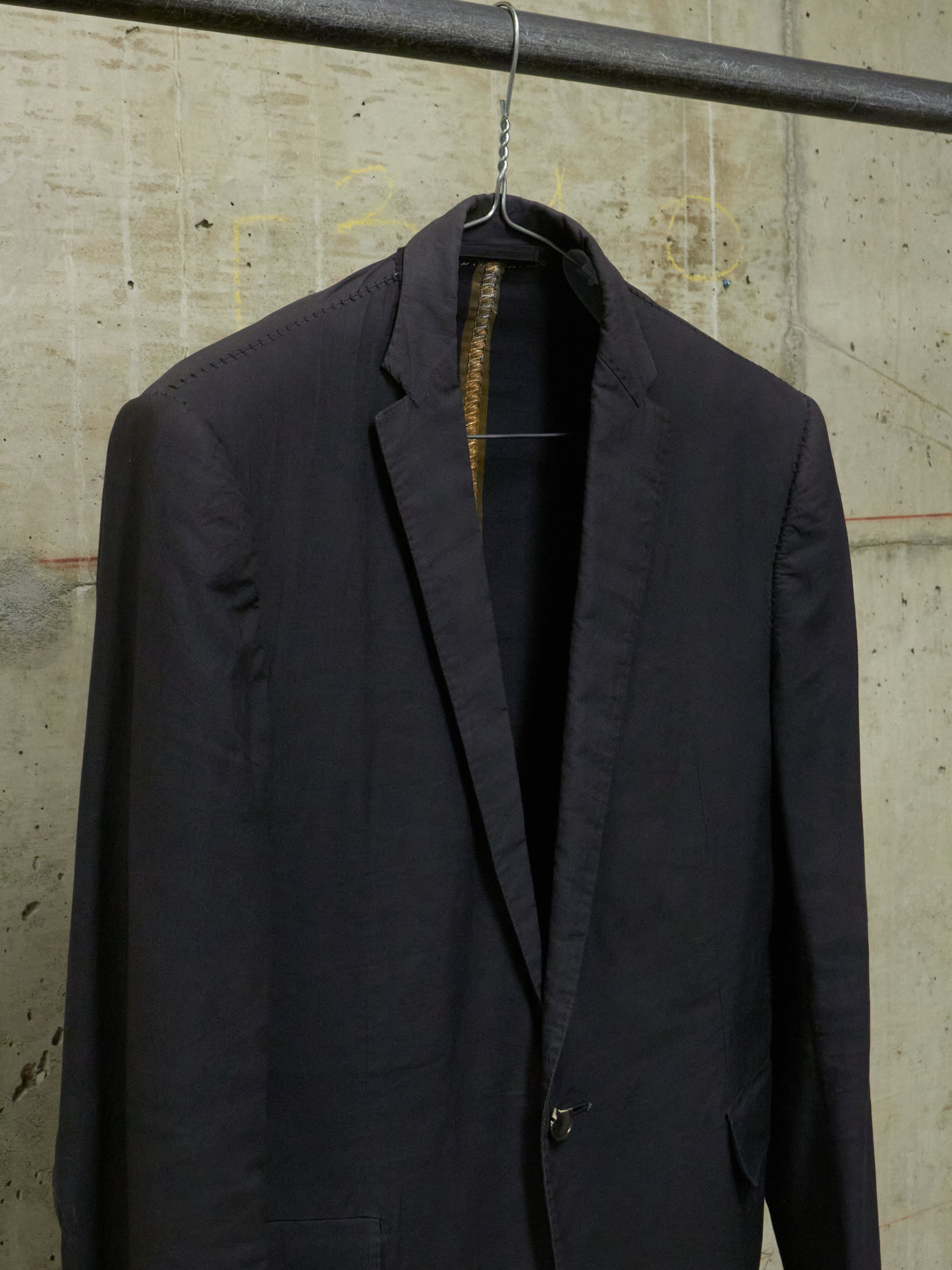 Black suit jacket hanging on a hook against a textured wall.
