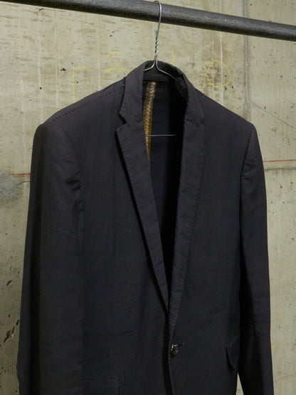 Black suit jacket hanging on a hook against a textured wall.