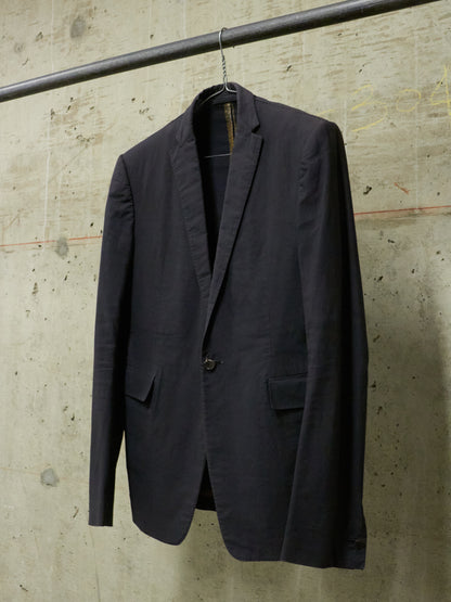Dark gray blazer hanging on a hook against a textured concrete wall.