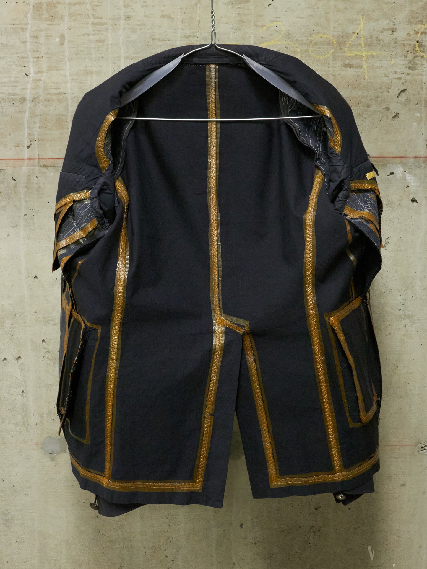 Black coat with gold accents on a hanger against a textured wall.
