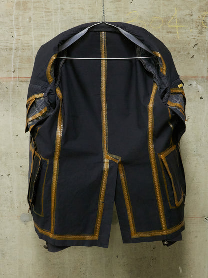Black coat with gold accents on a hanger against a textured wall.
