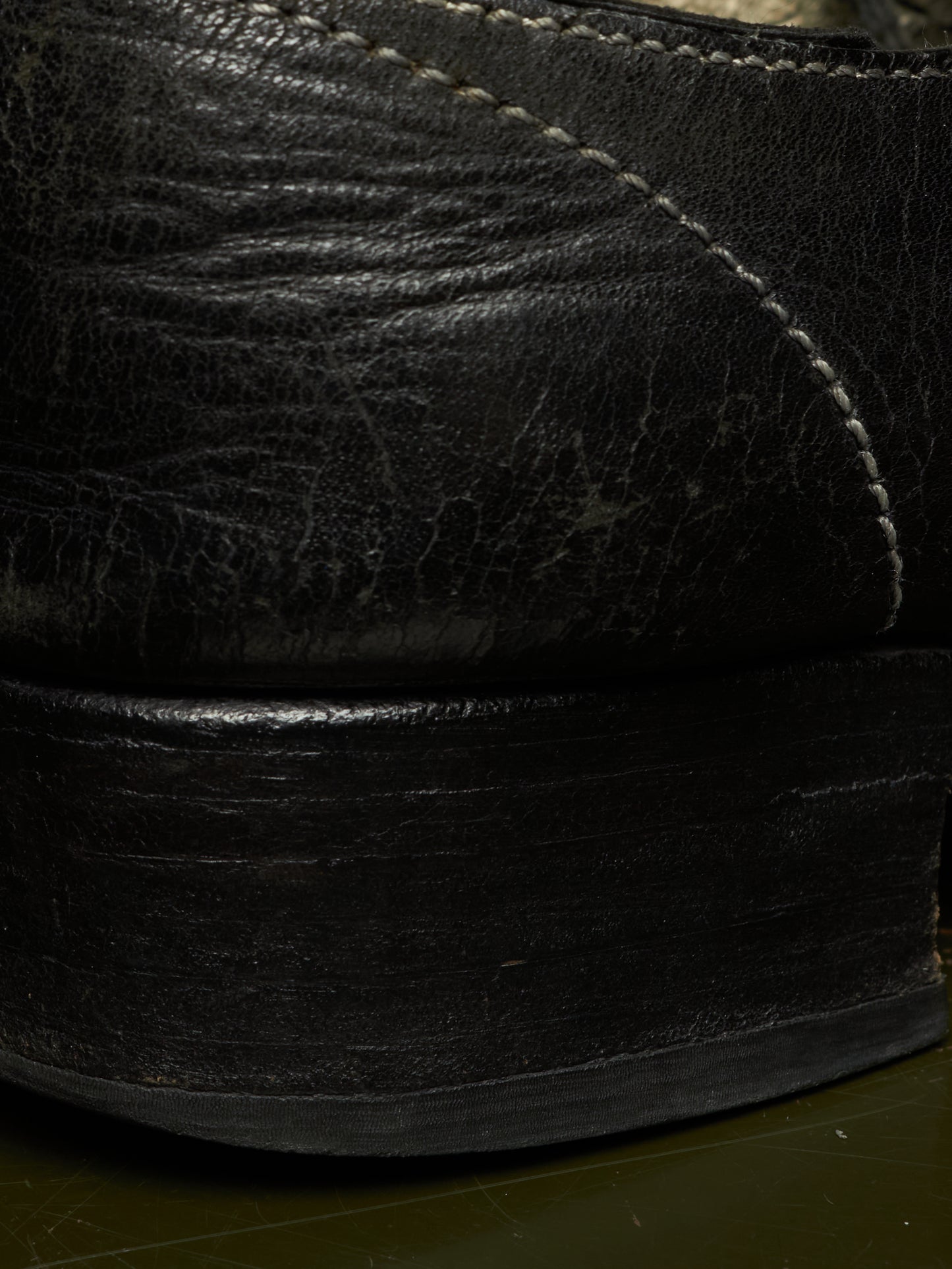 Close-up detail of a black leather shoe showing the textured leather upper, contrast stitching, and a thick black sole.