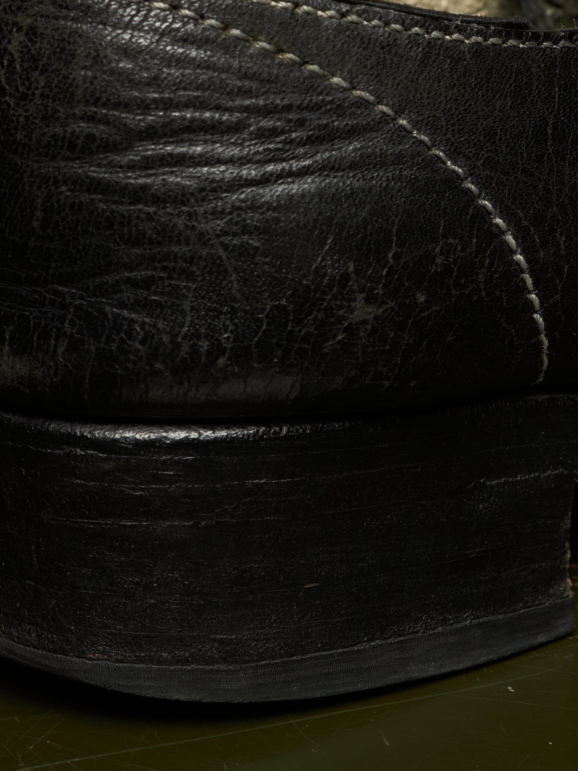 Close-up detail of a black leather shoe showing the textured leather upper, contrast stitching, and a thick black sole.