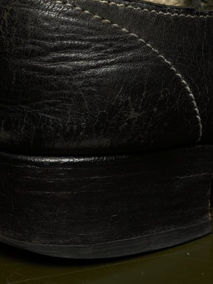 Close-up detail of a black leather shoe showing the textured leather upper, contrast stitching, and a thick black sole.