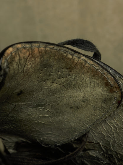 A close-up of a dark, distressed leather item showing the textured interior lining with visible cracks, scuffs, and a dark strap against a muted beige background.