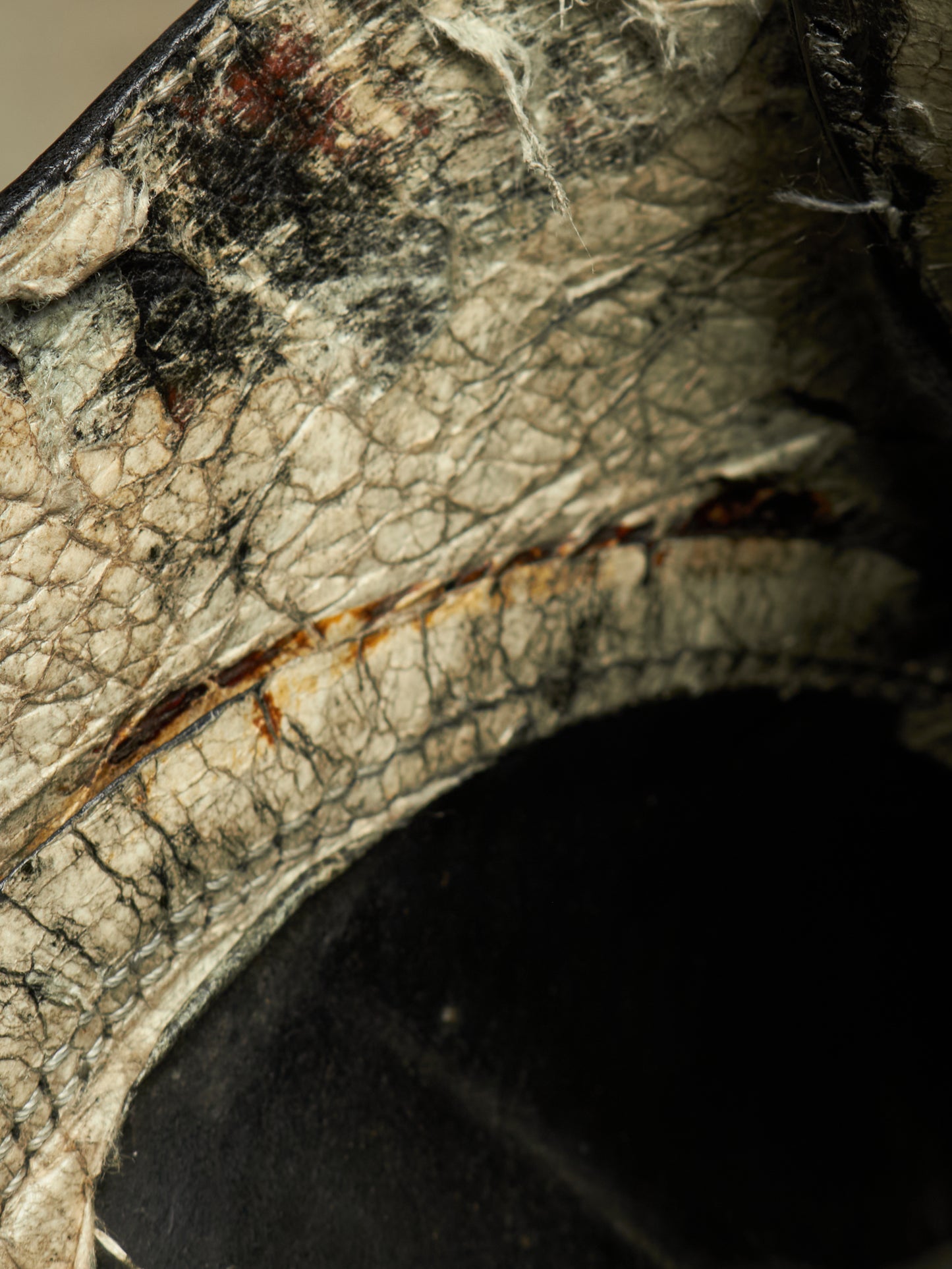 Close-up detail of a distressed leather or faux-leather surface with cracked texture, dark patches, and a curved black opening below.