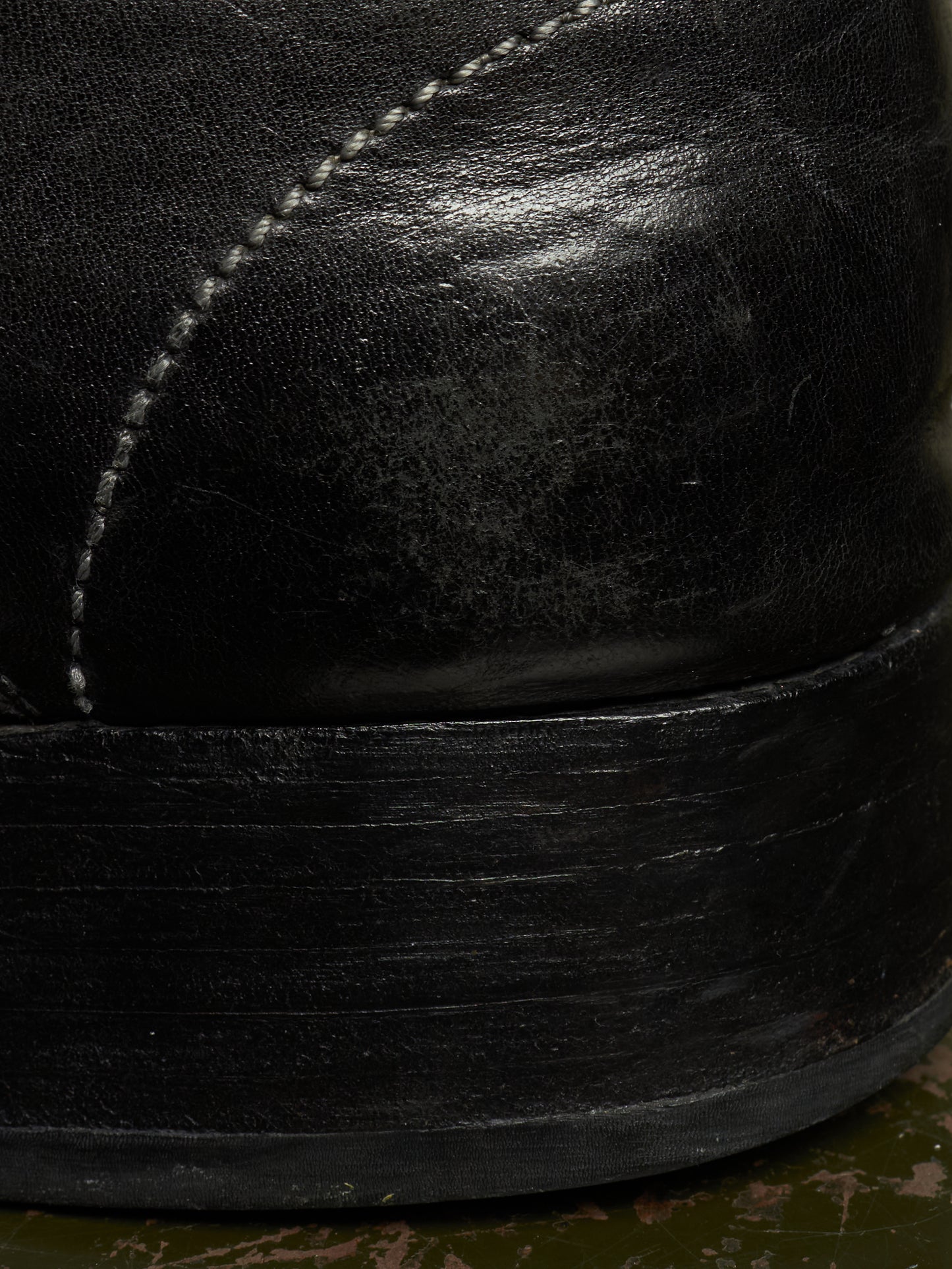 Close-up detail of a black leather boot showing the side panel with white stitching and the thick black rubber sole.