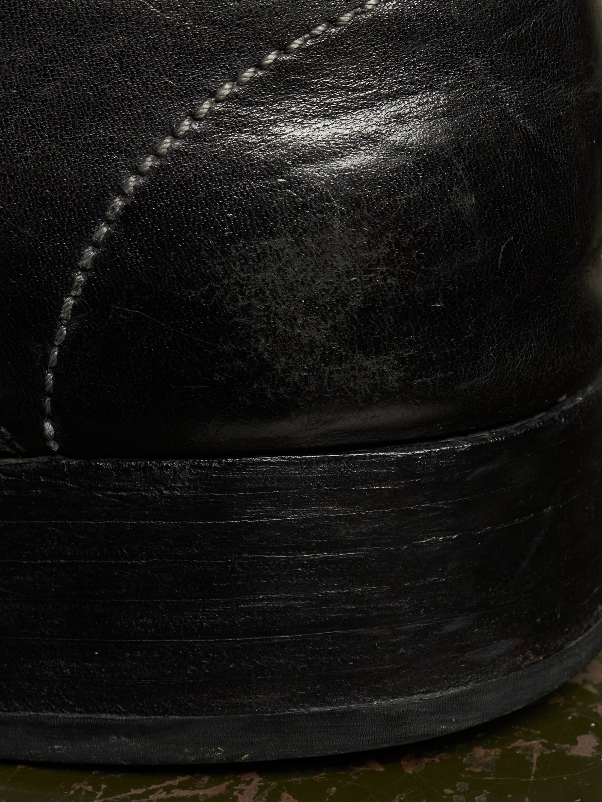 Close-up detail of a black leather boot showing the side panel with white stitching and the thick black rubber sole.