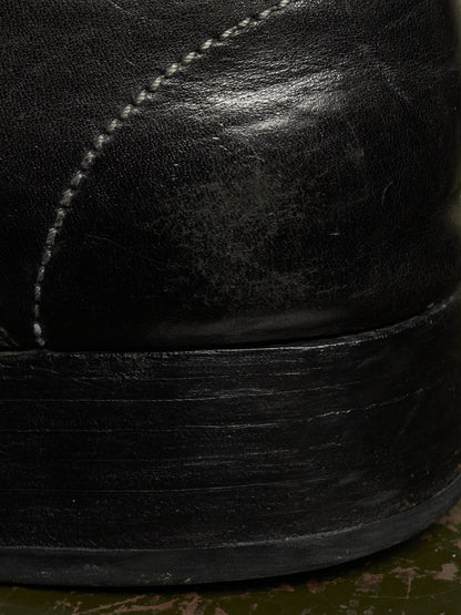 Close-up detail of a black leather boot showing the side panel with white stitching and the thick black rubber sole.