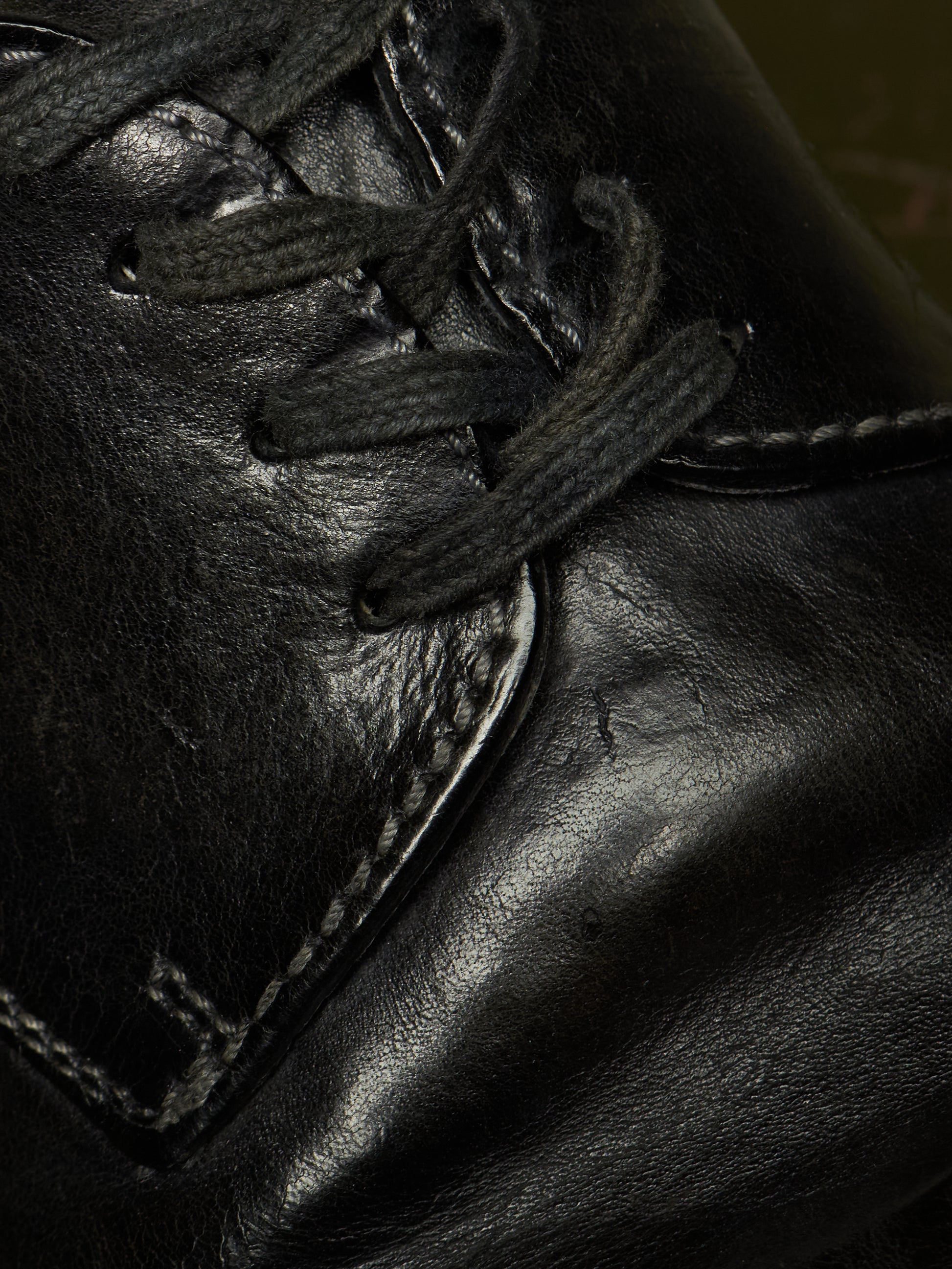 Close-up detail of a black leather lace-up shoe showing the laces, stitching, and textured leather surface.