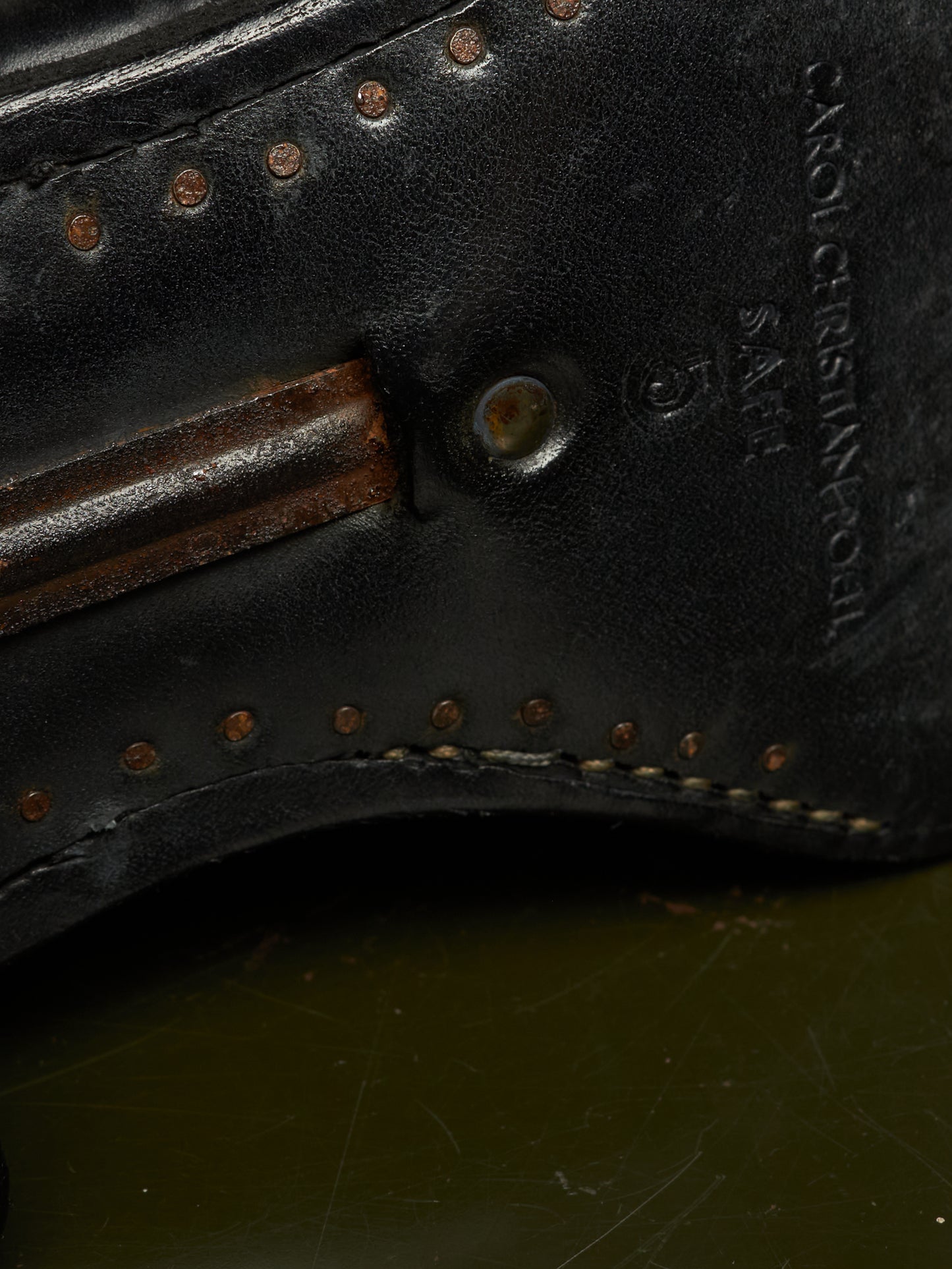 Close-up detail of a black leather shoe sole showing decorative brass-toned rivets, stitching, a metal eyelet, and embossed branding text reading 'CROCECINTA' and 'SABE'.