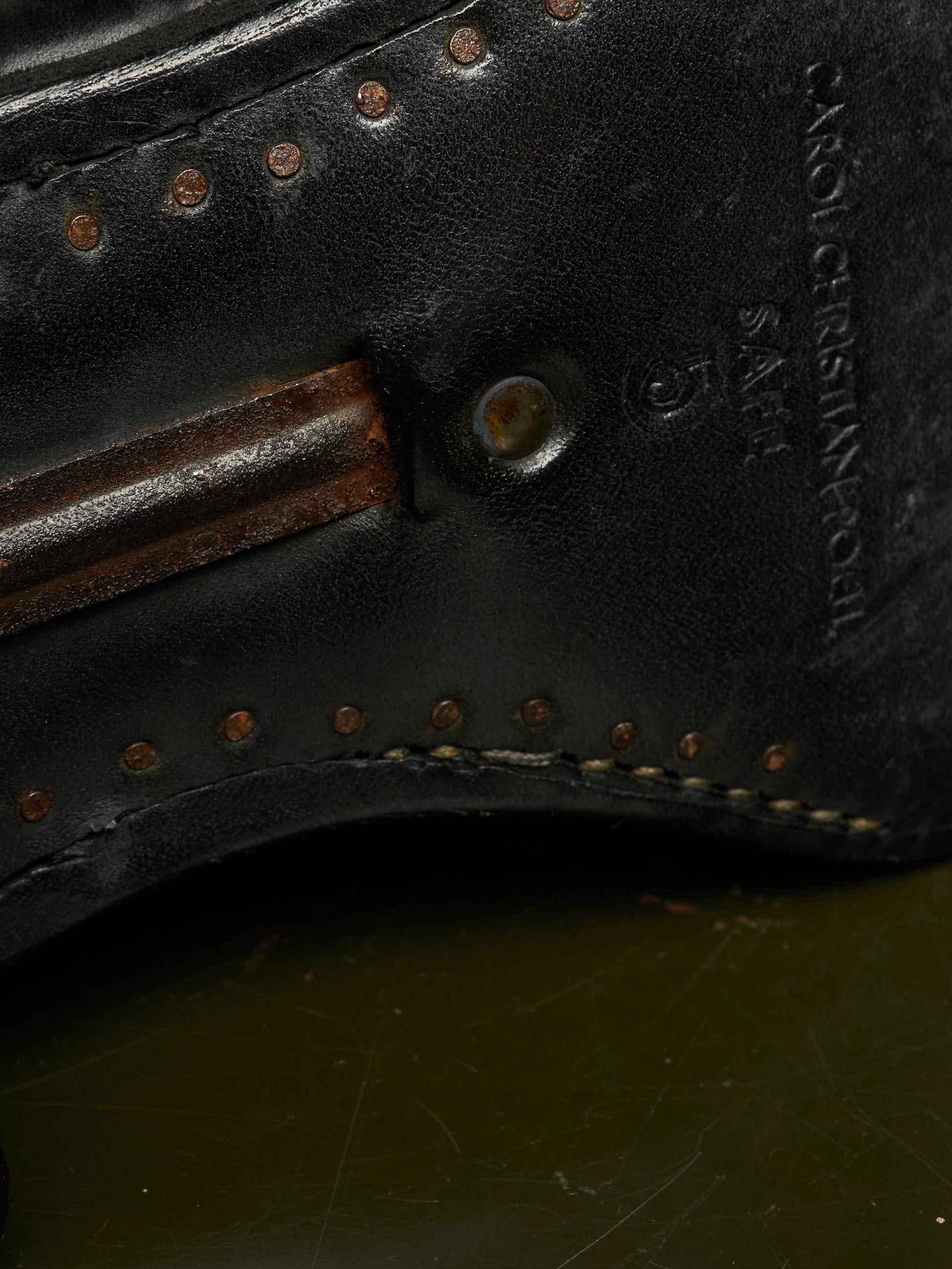 Close-up detail of a black leather shoe sole showing decorative brass-toned rivets, stitching, a metal eyelet, and embossed branding text reading 'CROCECINTA' and 'SABE'.