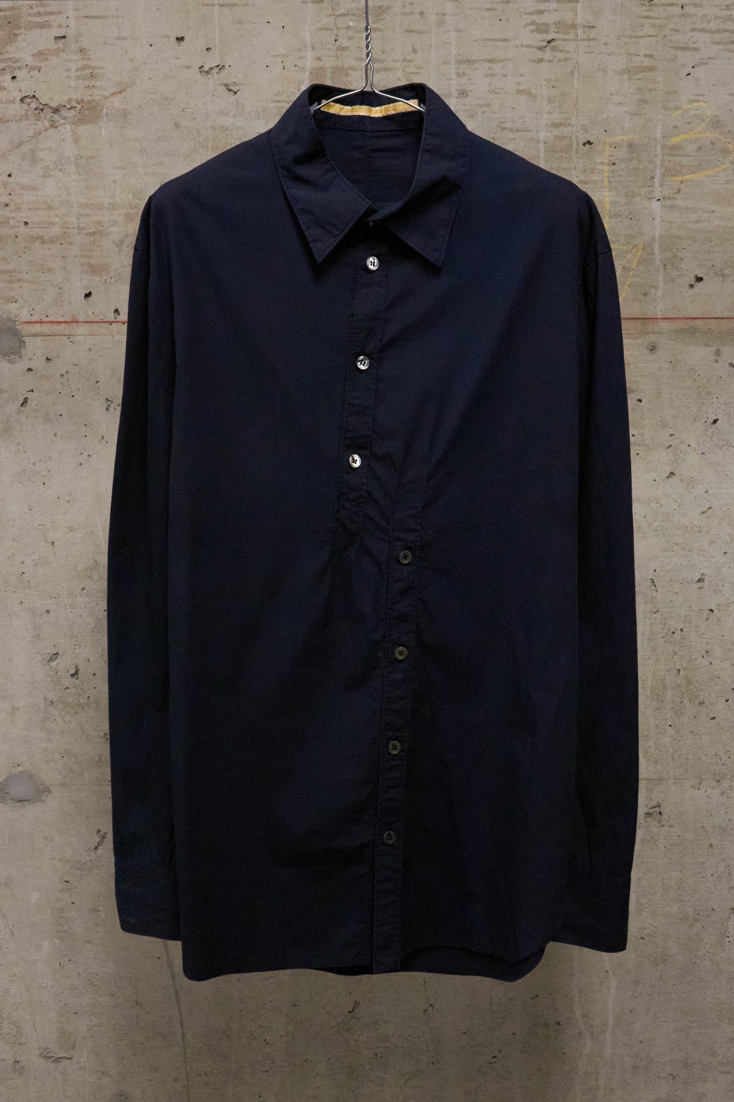 Navy blue shirt on a hanger against a textured beige wall