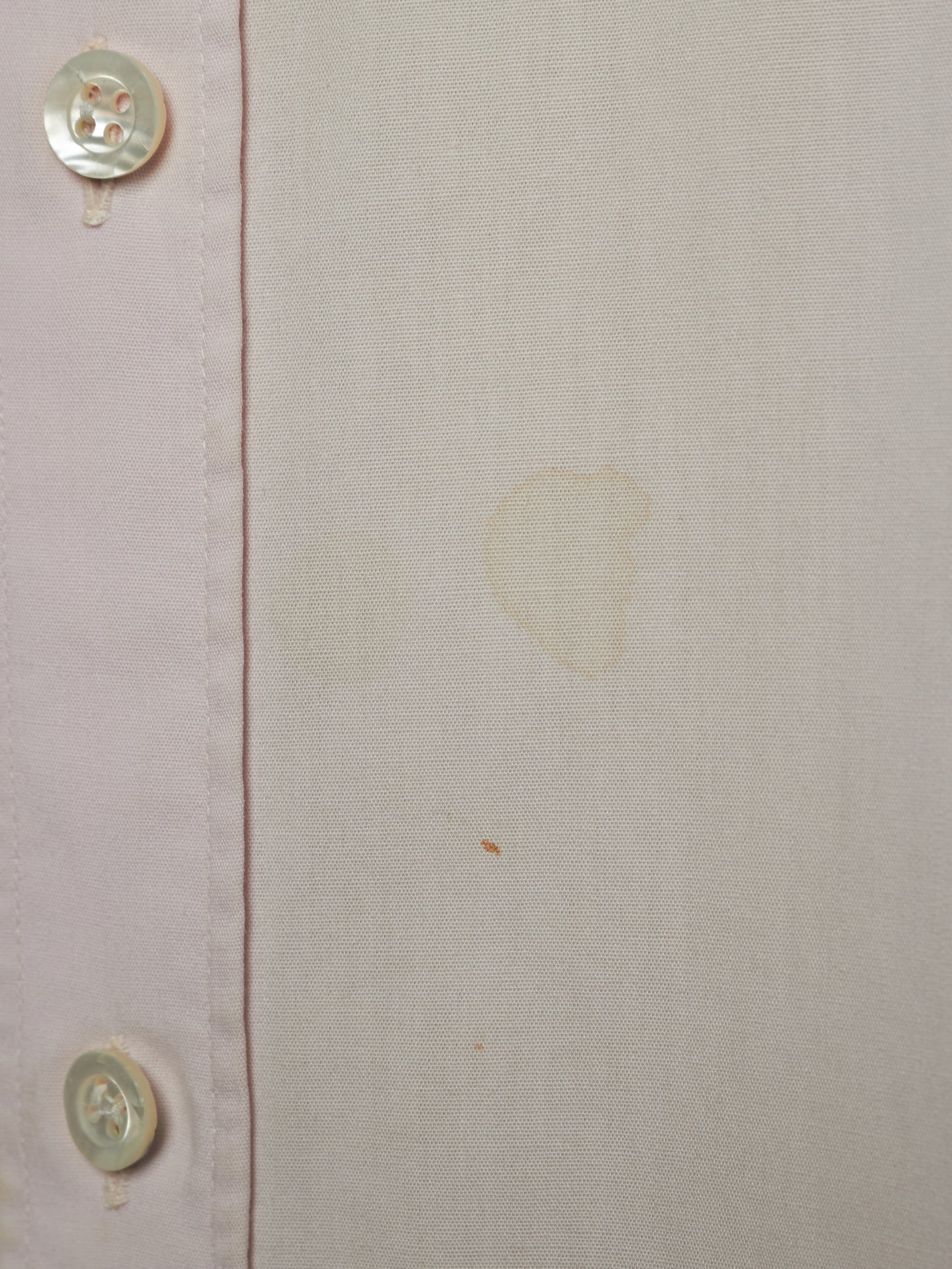 Close-up of a light beige or off-white linen-like fabric with a vertical seam and two visible buttons on the left edge. There are faint yellowish stains or marks on the fabric surface.