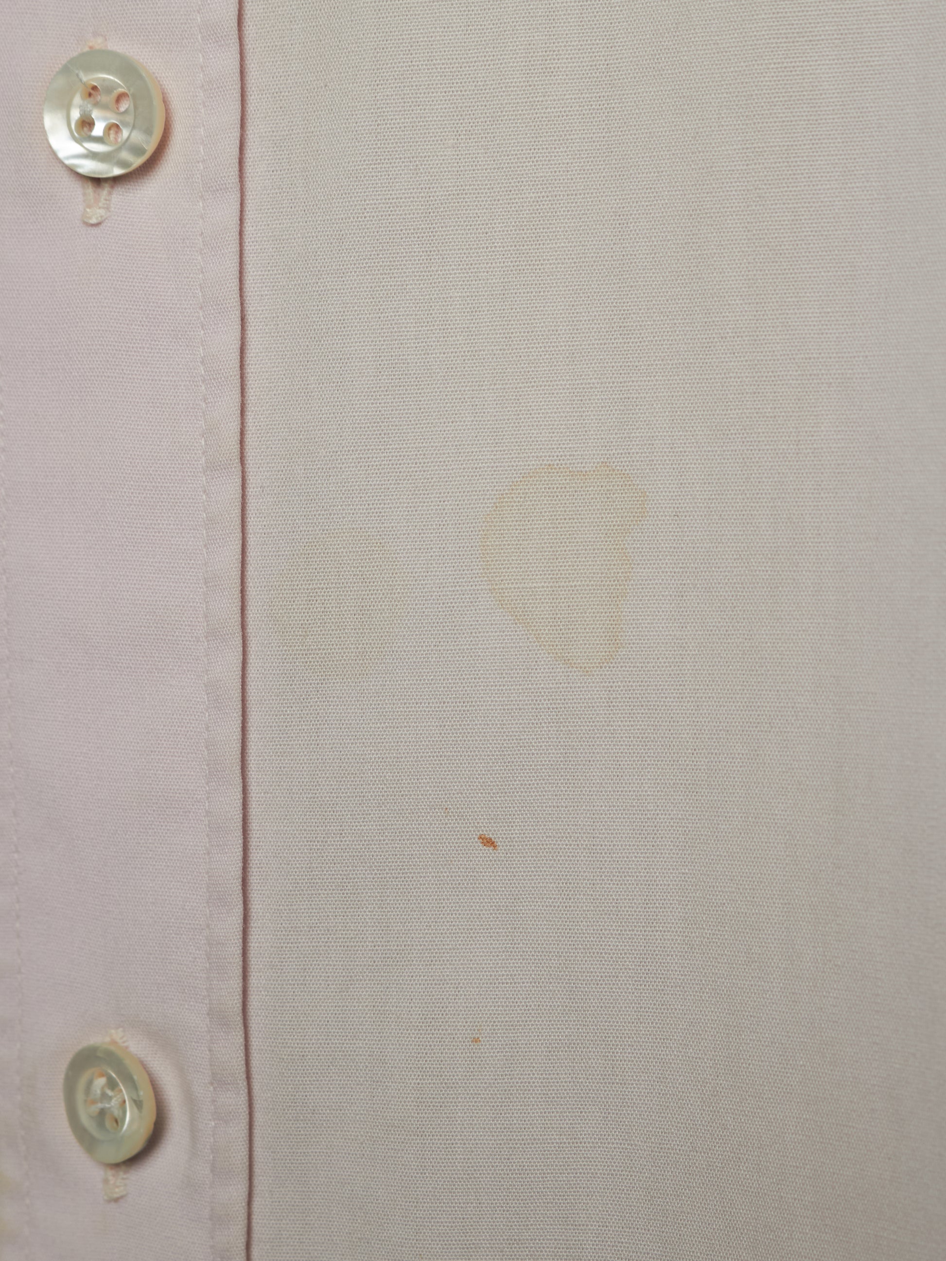 Close-up of a light beige or off-white linen-like fabric with a vertical seam and two visible buttons on the left edge. There are faint yellowish stains or marks on the fabric surface.
