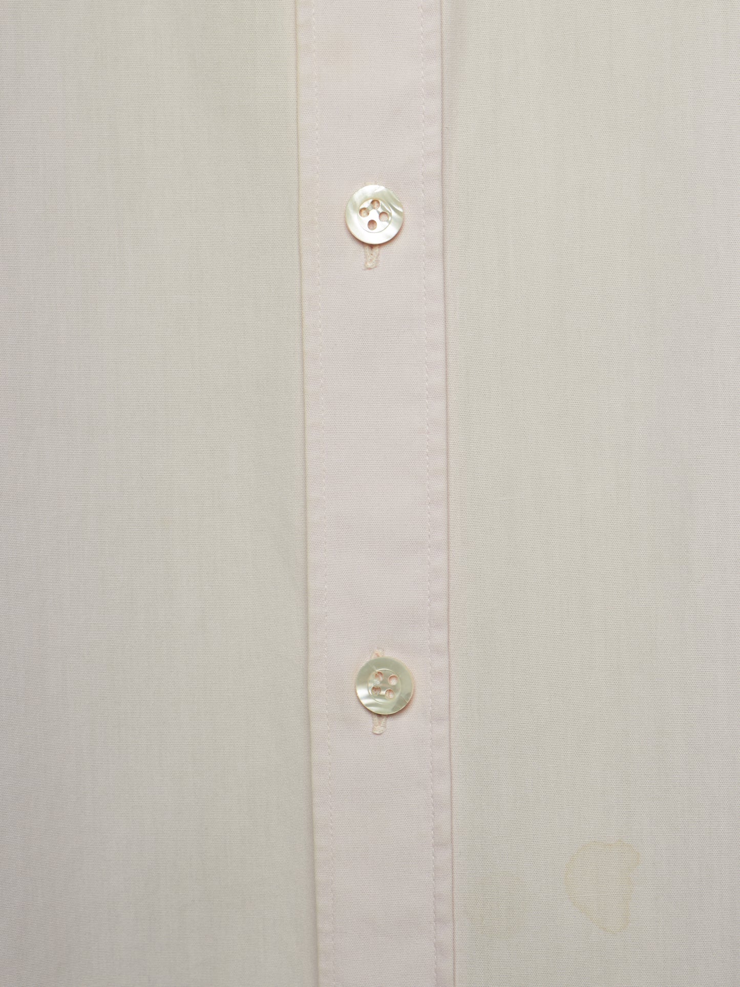 Close-up of a light cream or off-white button-down shirt showing the front placket with two round buttons.