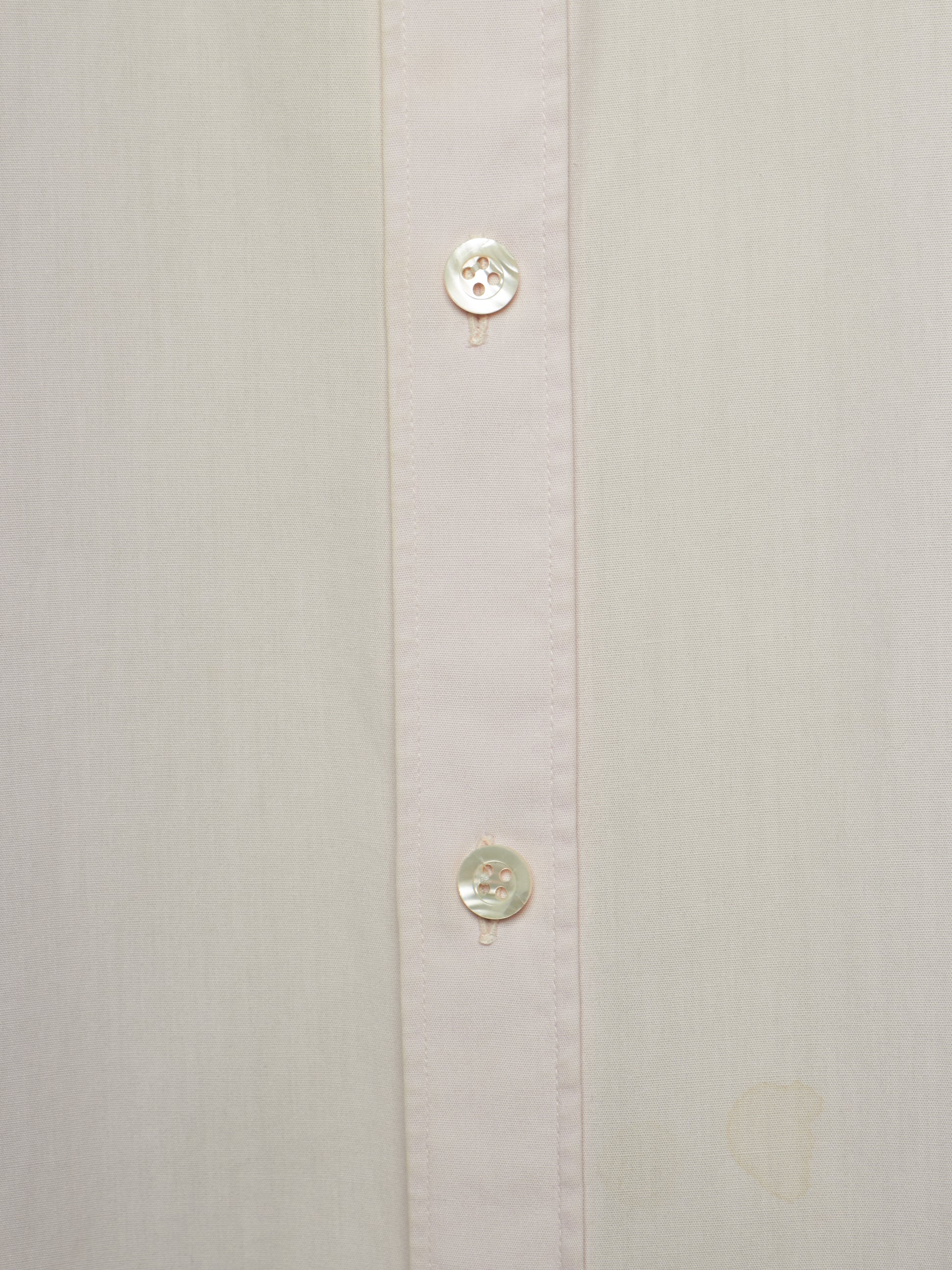 Close-up of a light cream or off-white button-down shirt showing the front placket with two round buttons.