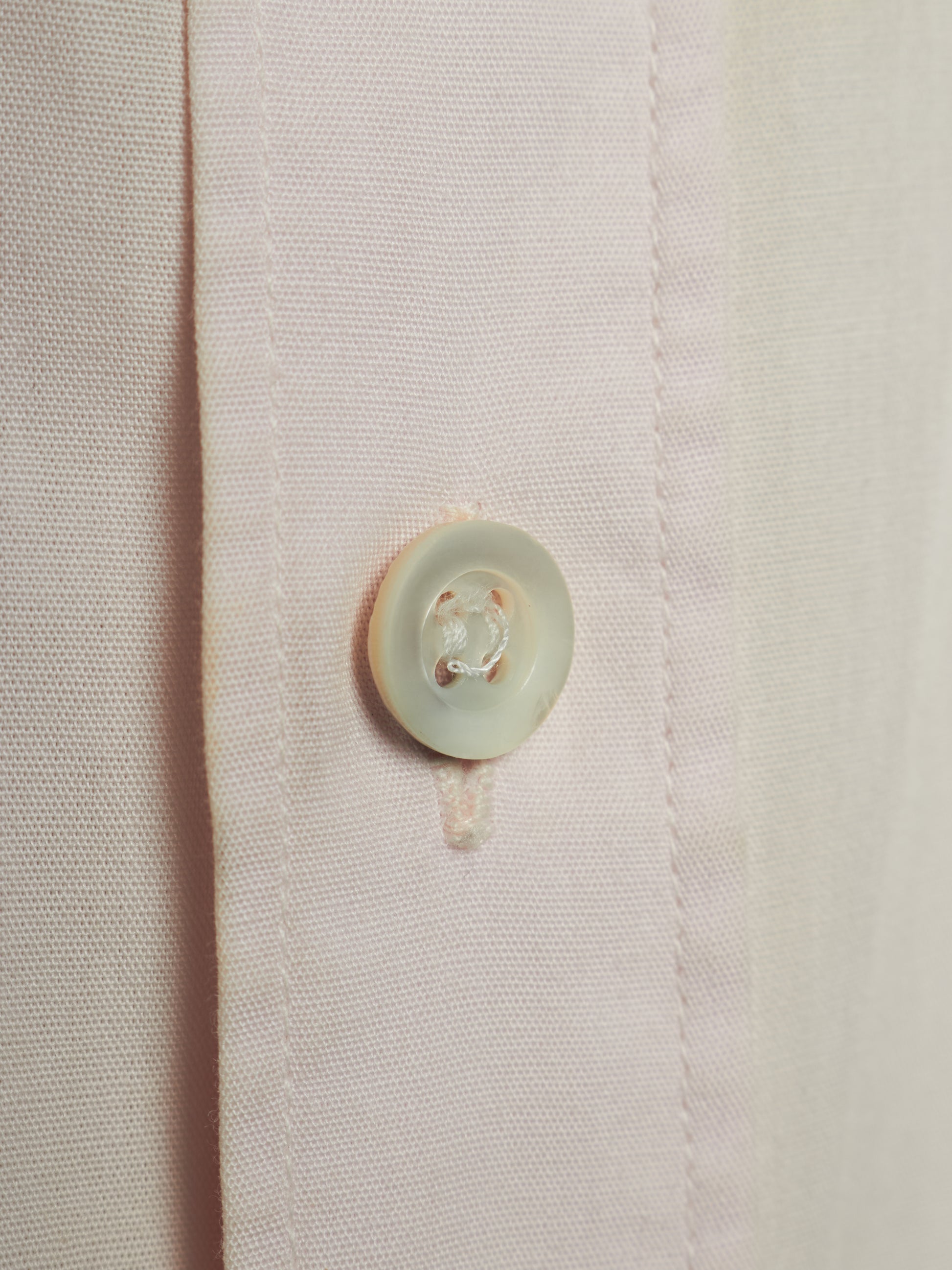 Close-up of a light pink or blush button-down shirt fabric with a single round off-white button on the front placket.