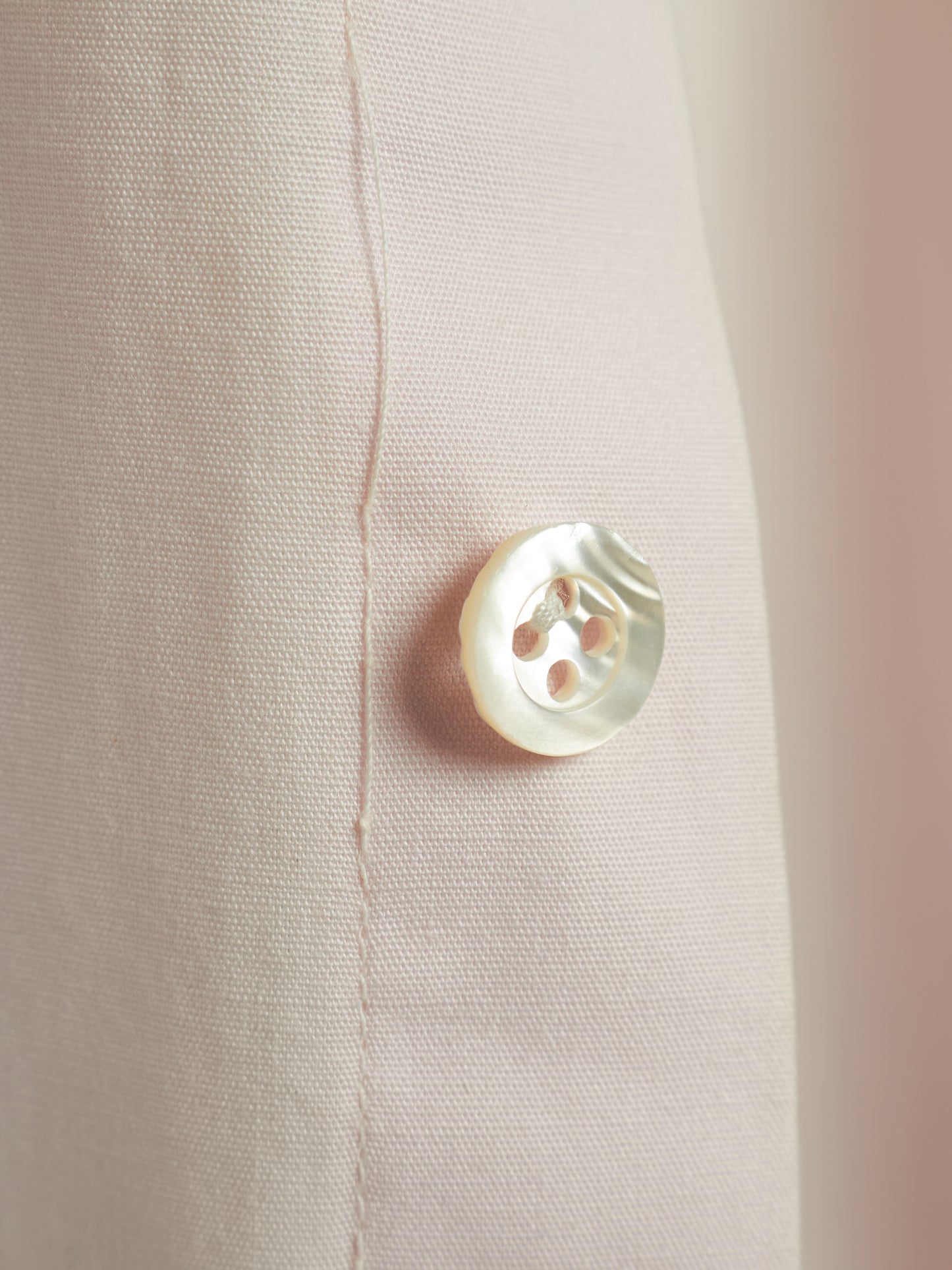 Close-up of a light beige textured fabric with a single round white mother-of-pearl button.