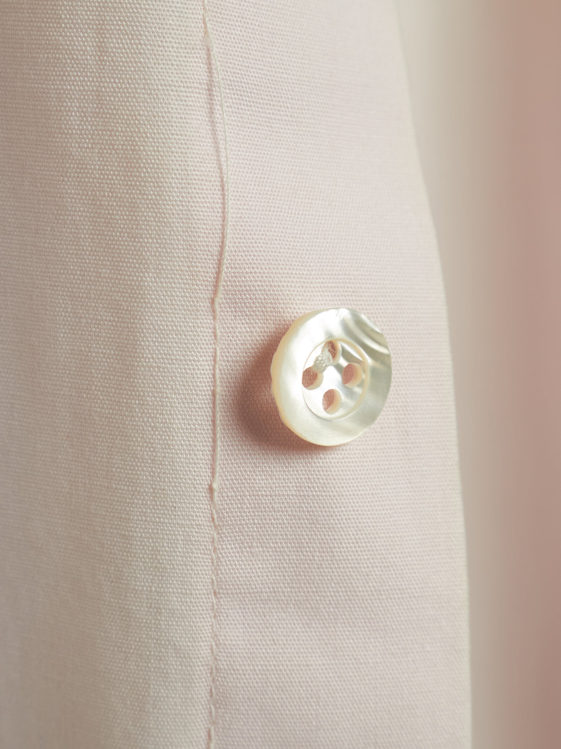 Close-up of a light beige textured fabric with a single round white mother-of-pearl button.