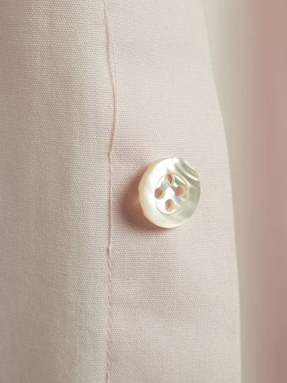 Close-up of a light beige textured fabric with a single round white mother-of-pearl button.