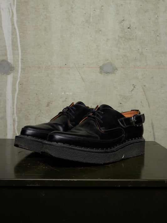 Pair of black leather shoes on a dark surface with a textured beige wall background