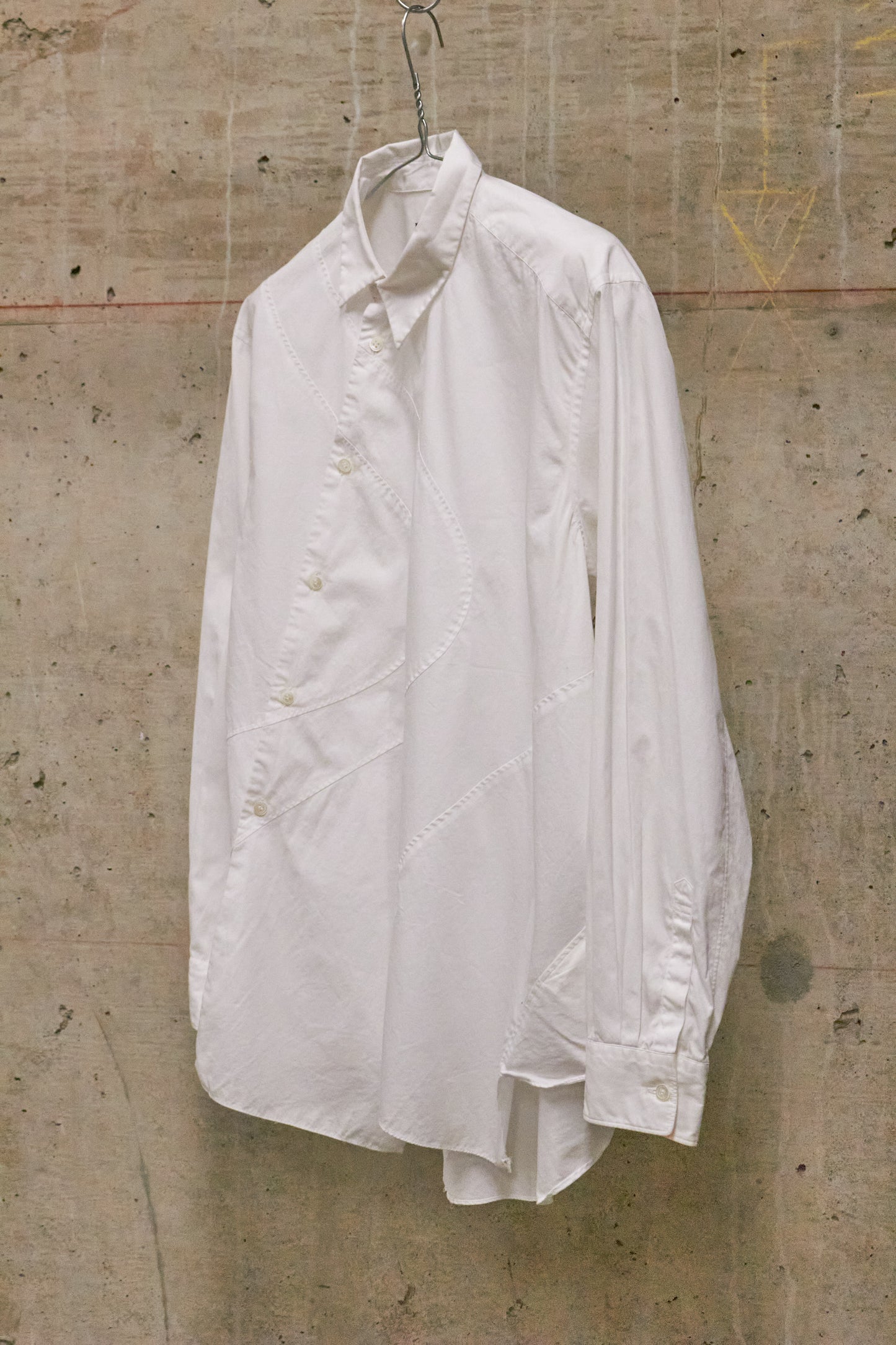 White shirt hanging on a hook against a textured concrete wall