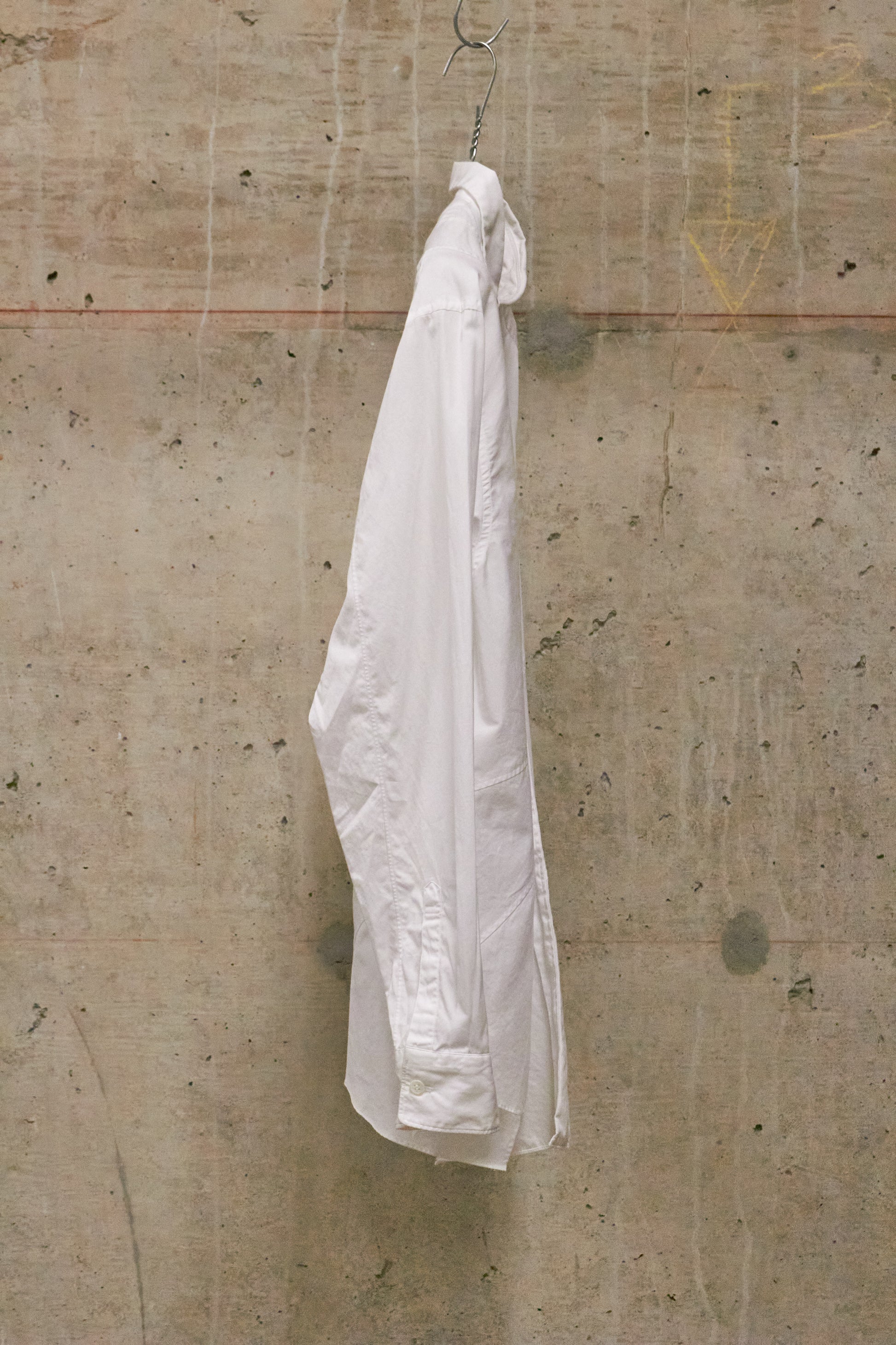 White shirt hanging on a hook against a textured beige wall.