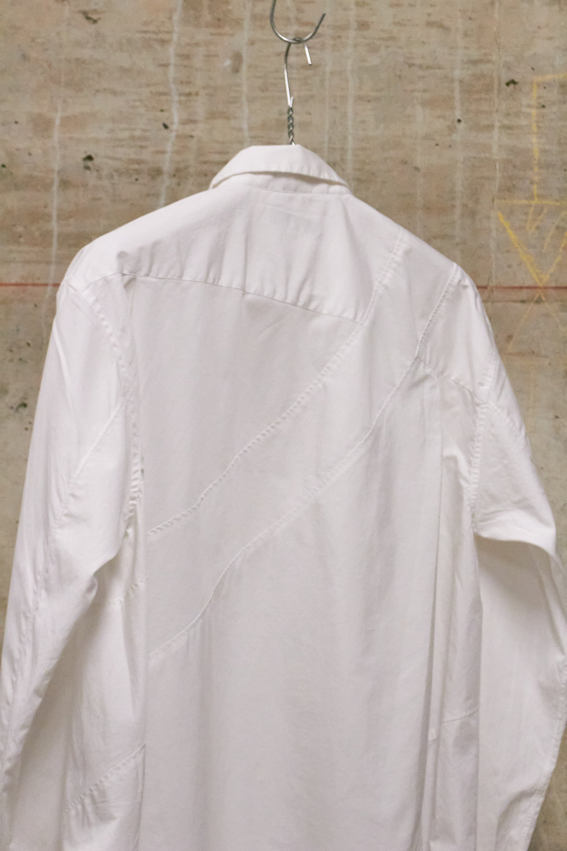 White shirt on a hanger against a textured wall.