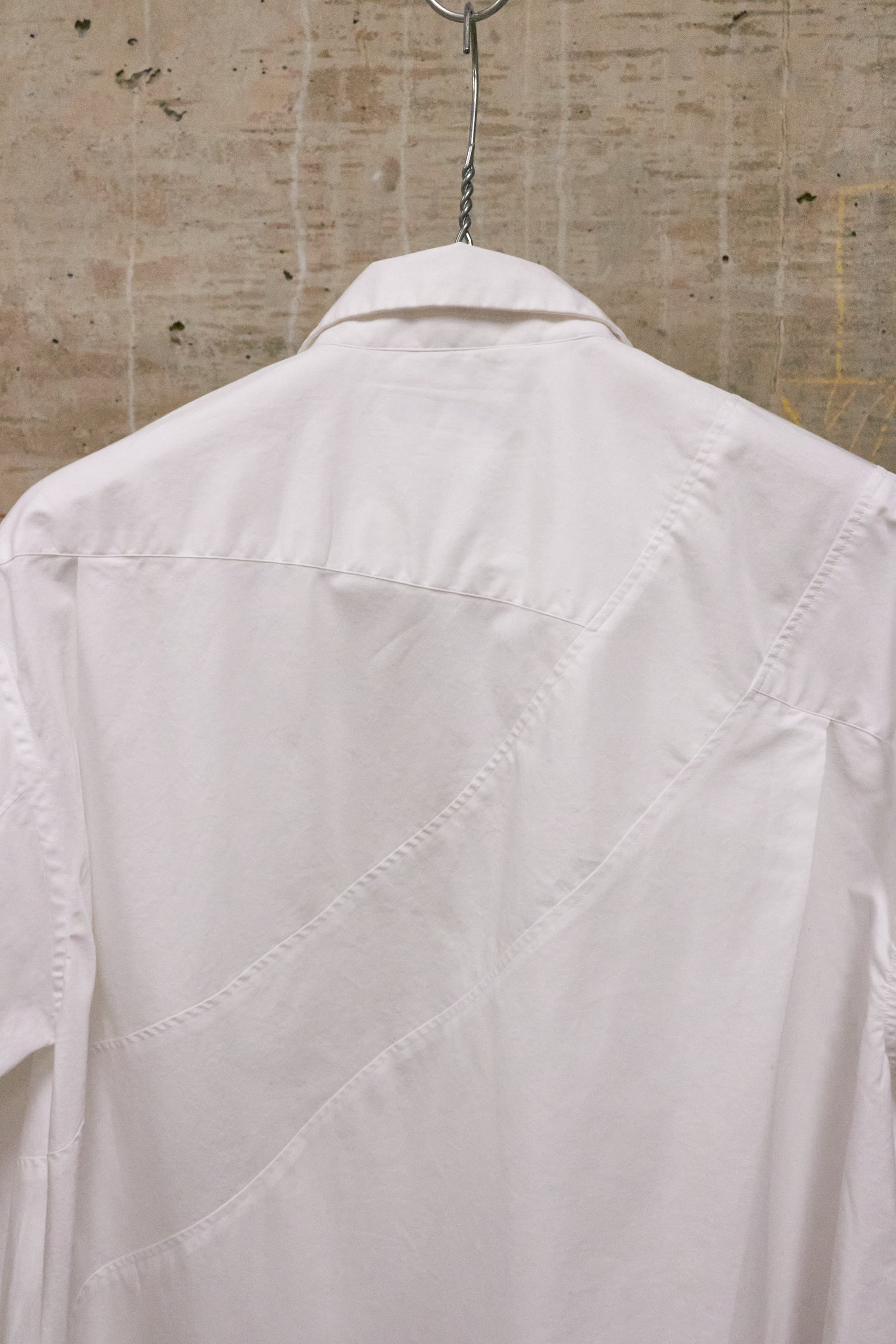 White shirt hanging on a hanger against a textured beige wall.