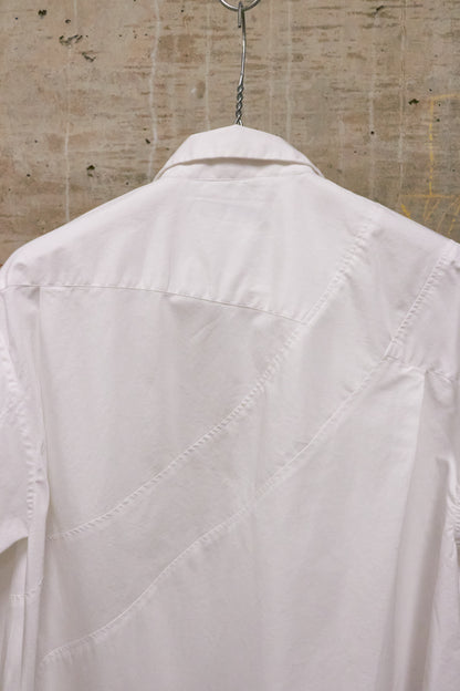 White shirt hanging on a hanger against a textured beige wall.