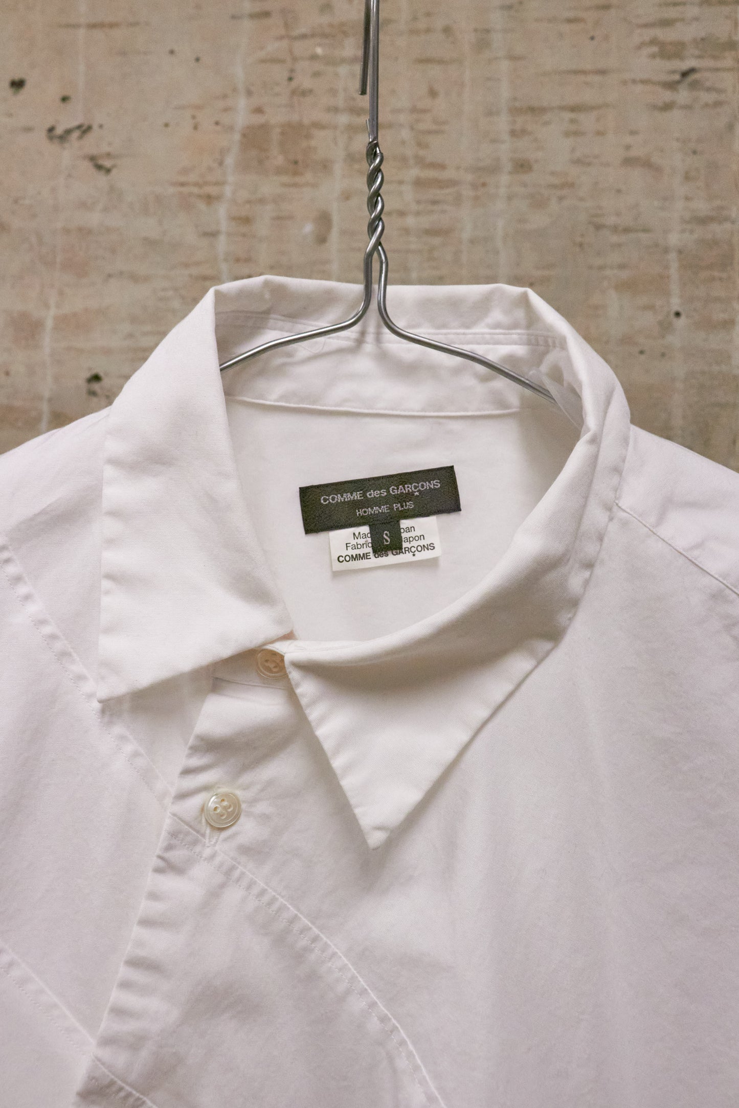 White shirt on a hanger with a visible label against a textured wall background