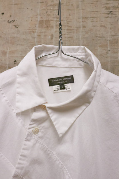 White shirt on a hanger with a visible label against a textured wall background
