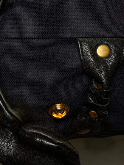 Close-up detail of a black canvas and leather bag featuring brass snap buttons and a braided leather strap.