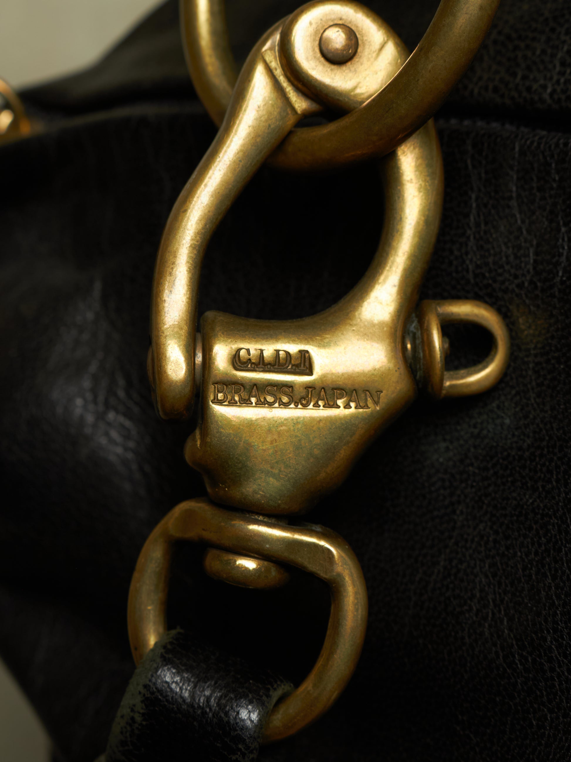 Close-up of a black leather bag featuring a prominent brass clasp engraved with 'CLM BRASS JAPAN'.