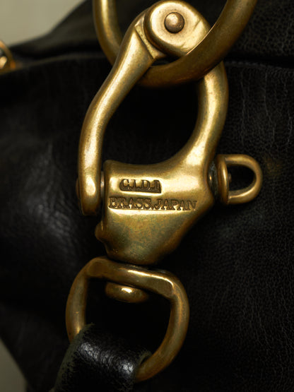 Close-up of a black leather bag featuring a prominent brass clasp engraved with 'CLM BRASS JAPAN'.