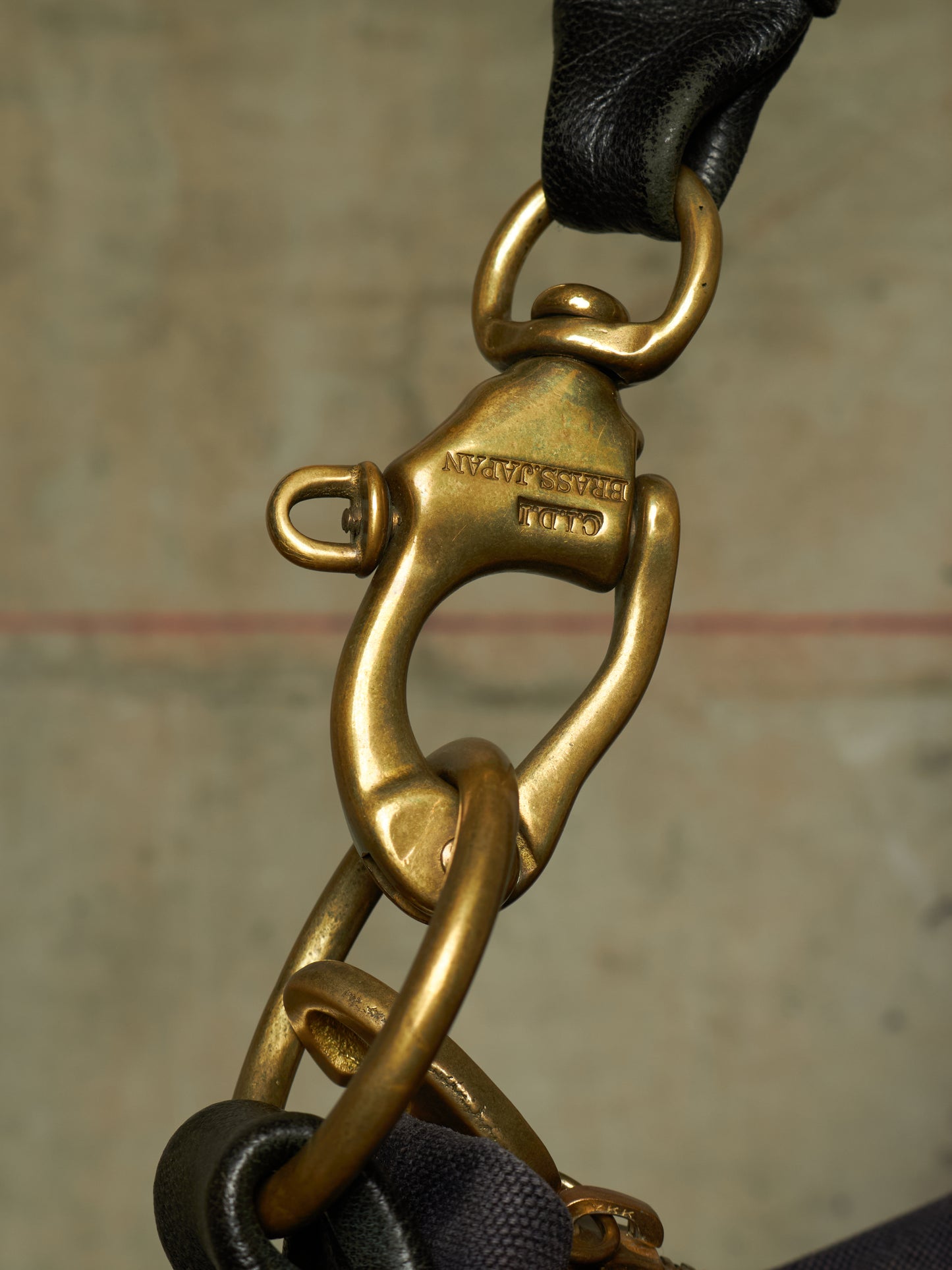 Close-up of a brass clasp and chain hardware attached to a black leather strap, with engraved text visible on the clasp.