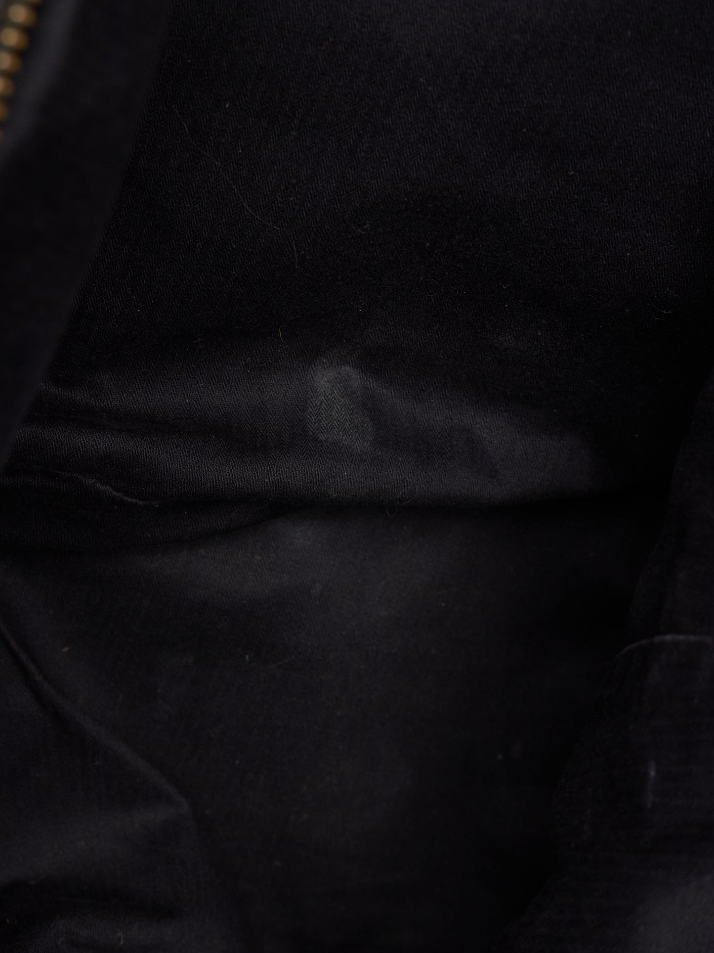 Close-up of a black fabric surface with soft folds and a small portion of a gold zipper visible at the top left edge.