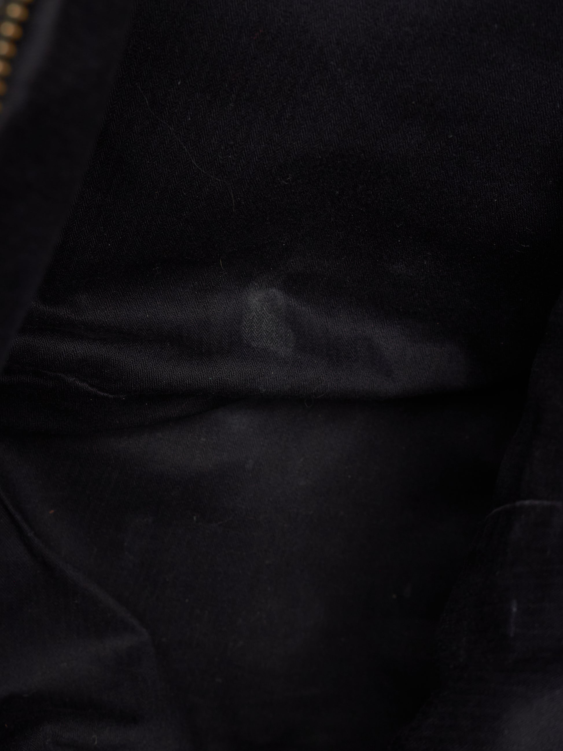 Close-up of a black fabric surface with soft folds and a small portion of a gold zipper visible at the top left edge.
