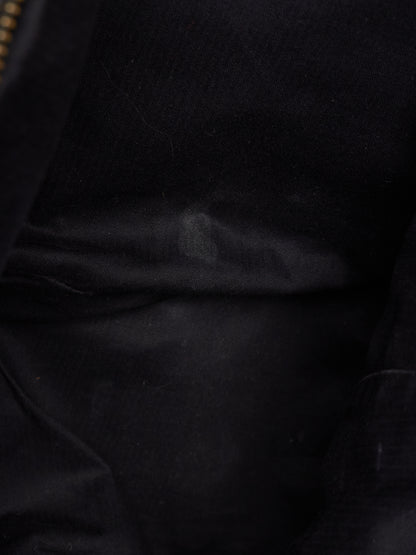 Close-up of a black fabric surface with soft folds and a small portion of a gold zipper visible at the top left edge.